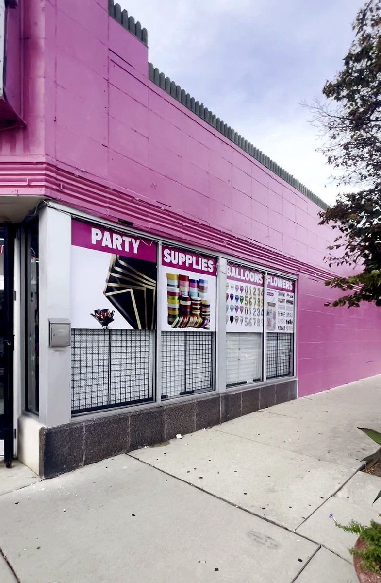 Pink brick storefront with printed window graphics reading Party Supplies and Balloons