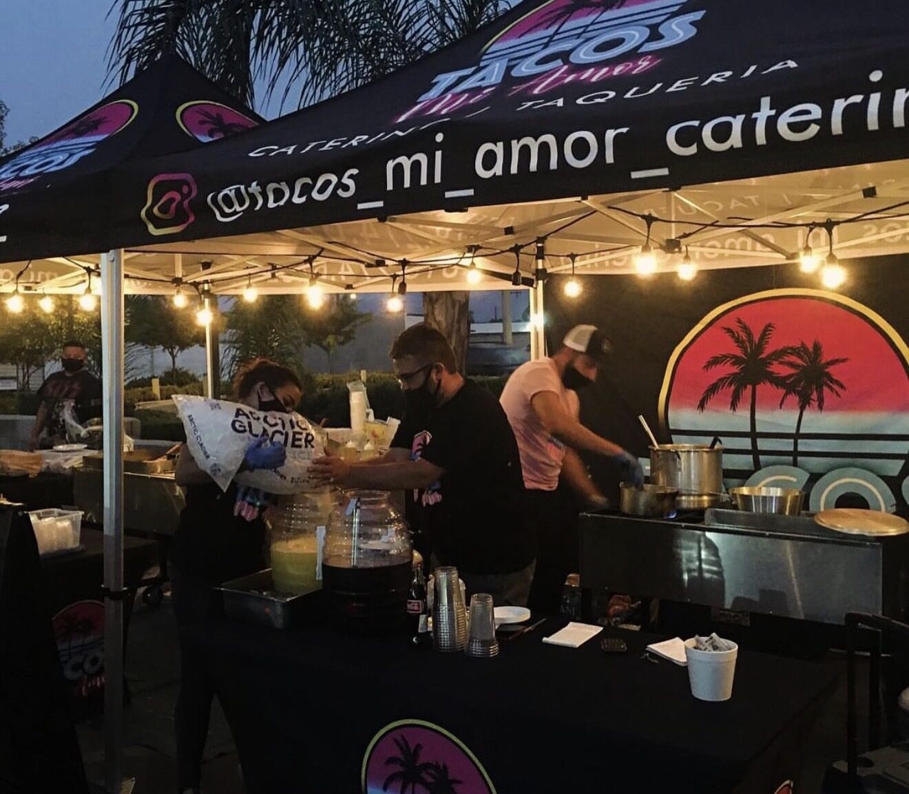 Catering crew working under a printed Tacos Mi Amor canopy at night